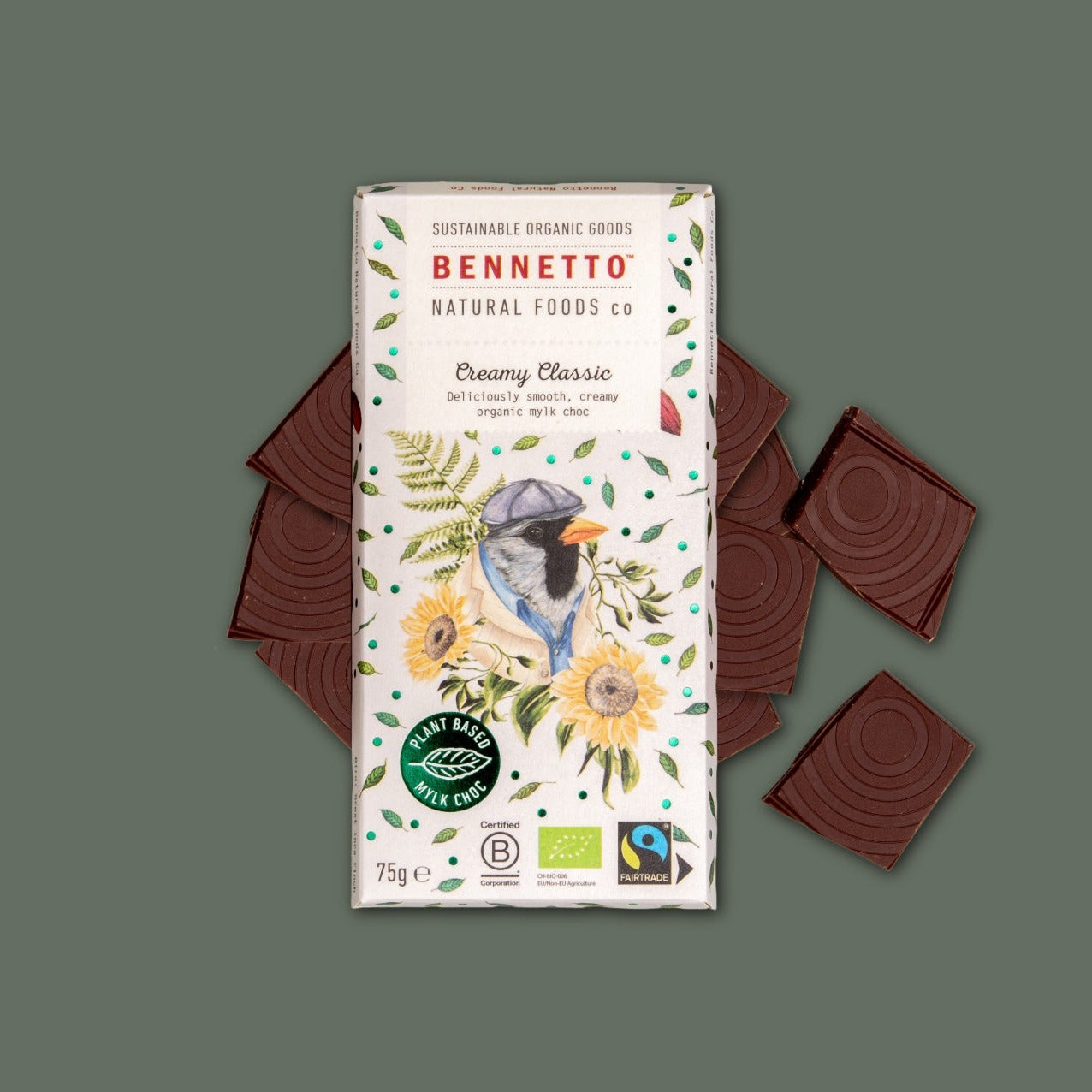A 75g bar of Bennett's Natural Foods Co. 'Creamy Classic' chocolate, shown in its illustrated white packaging with a bird and yellow flowers, surrounded by four dark brown chocolate squares on a muted green background.